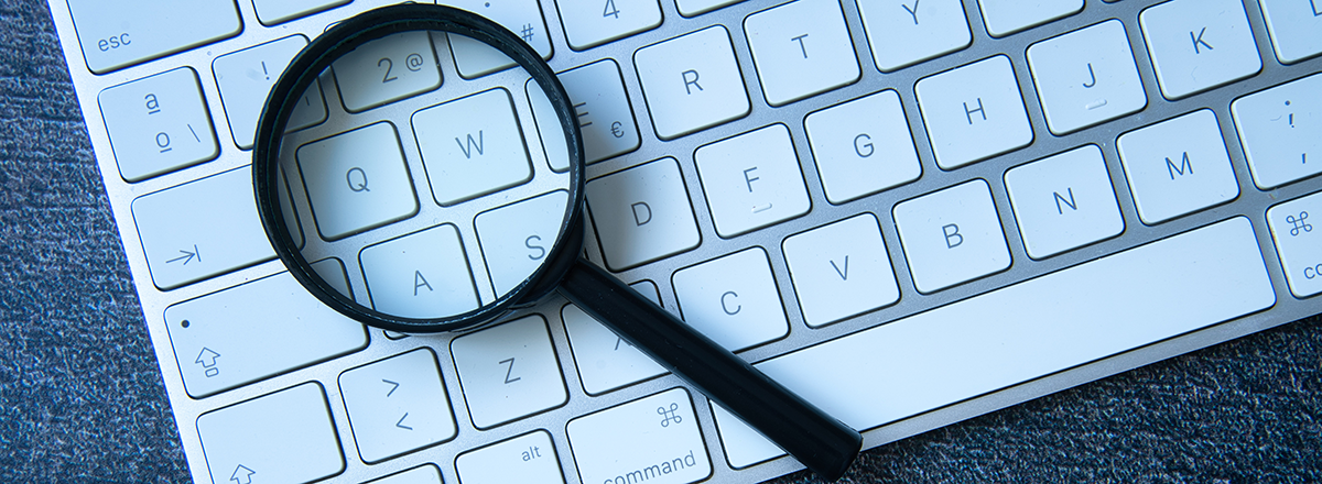 A magnifying glass on top of a Mac keyboard lying on the keys.