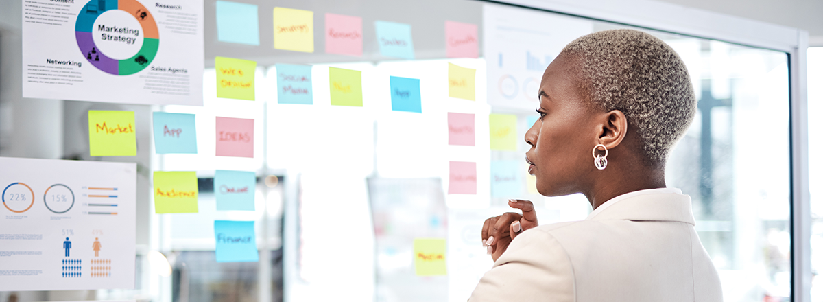 A woman looks at a whiteboard with sticky notes of marketing ideas.