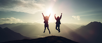 Two people jumping into the air on a mountain.